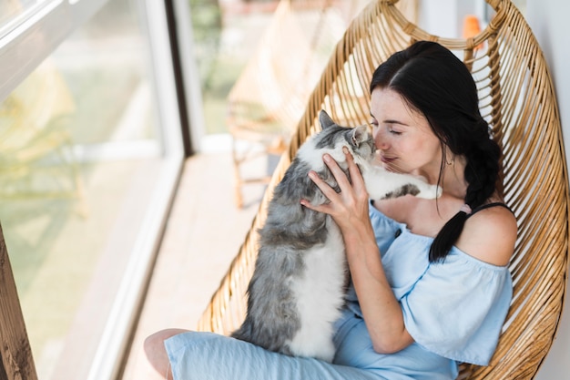 Bella giovane donna che si siede sulla sedia di legno al patio che ama il suo gatto