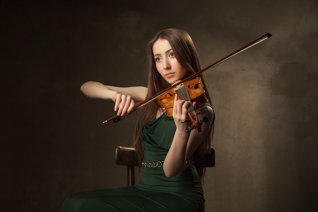 Bella giovane donna che suona il violino su sfondo nero