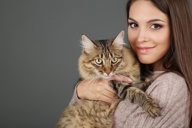 Bella giovane donna che tiene gatto su sfondo grigio