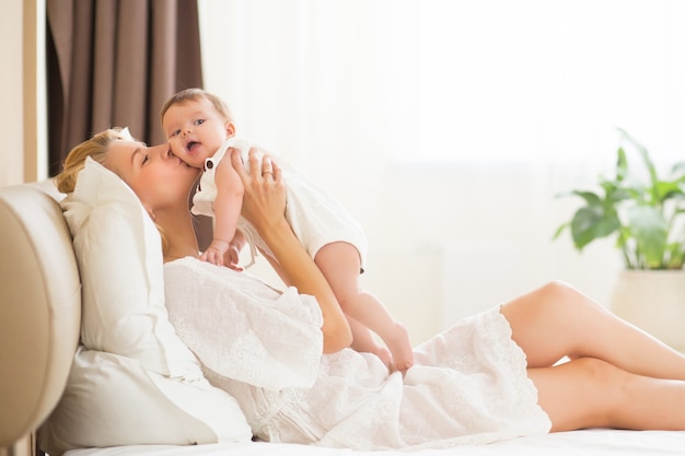 Bella giovane donna che tiene la bambina tra le braccia nella stanza domestica al mattino