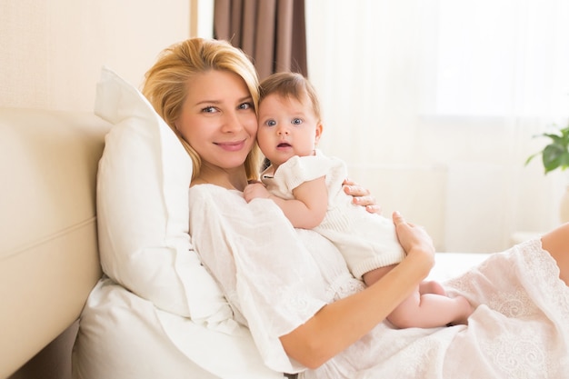 Bella giovane donna che tiene la bambina tra le braccia nella stanza domestica al mattino