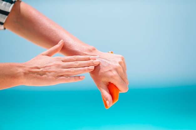 Bella giovane donna che tiene una crema solare che si trova sulla spiaggia tropicale