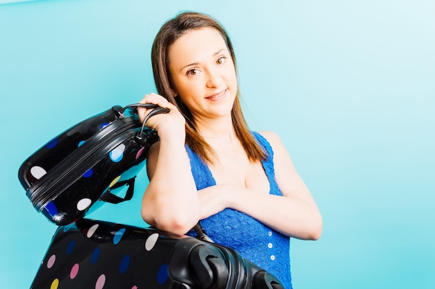 Bella giovane donna che tiene valigia e borsa da toilette da viaggio con sfondo blu. concetto di viaggio