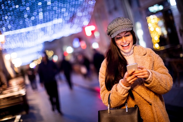 Bella giovane donna che usa il suo telefono cellulare in strada a Natale