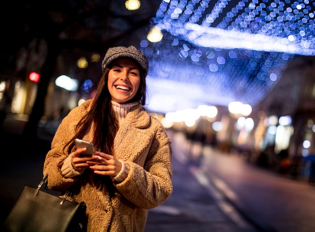 Bella giovane donna che usa il suo telefono cellulare in strada a Natale
