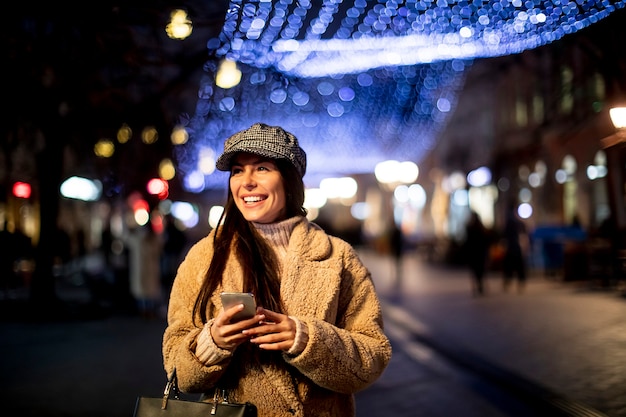 Bella giovane donna che usa il suo telefono cellulare in strada a Natale