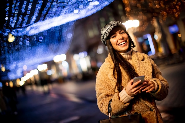 Bella giovane donna che usa il suo telefono cellulare in strada a Natale