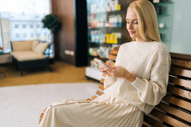 Bella giovane donna che usa lo smartphone guardando sullo schermo leggendo messaggi di testo e comunicando sui social network sulla panchina