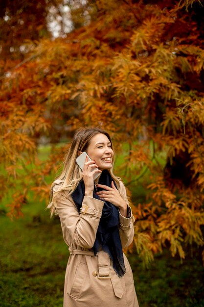 Bella giovane donna che utilizza il telefono cellulare nella sosta di autunno