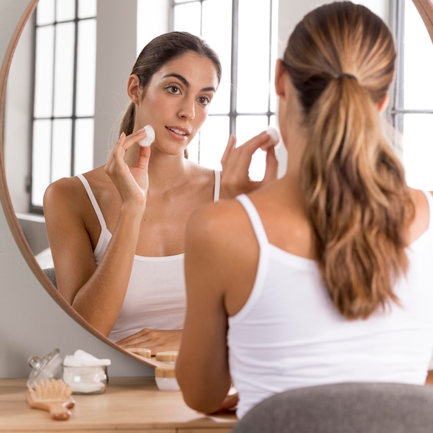 Bella giovane donna che utilizza la crema da giorno a casa