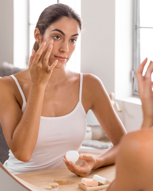 Bella giovane donna che utilizza la crema da giorno a casa