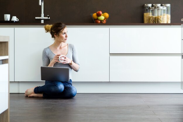 Bella giovane donna che utilizza la sua compressa digitale in cucina a casa.