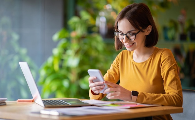 Bella giovane donna che utilizza laptop e smartphone al caffè