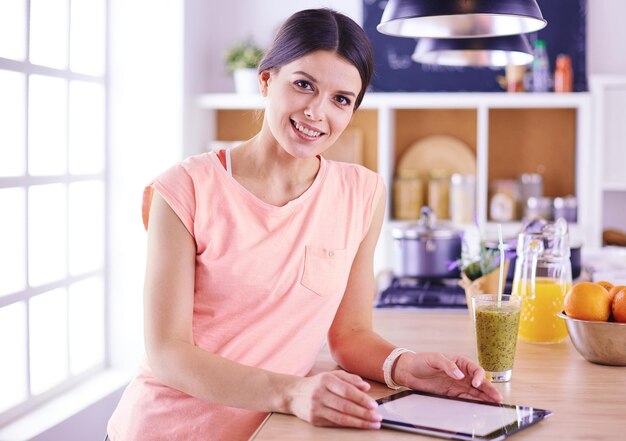 Bella giovane donna che utilizza una tavoletta digitale in cucina