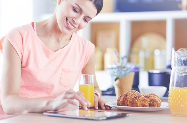 Bella giovane donna che utilizza una tavoletta digitale in cucina