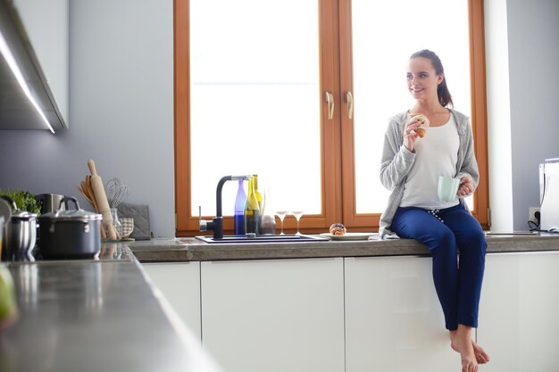 Bella giovane donna che utilizza una tavoletta digitale in cucina