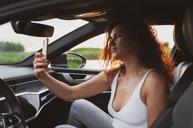 Bella giovane donna che viaggia sulle strade in auto ferma a lato delle fotografie stradali su uno smartphone