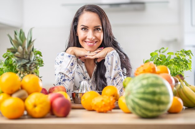 Bella giovane donna circondata da frutta esotica fresca in cucina.