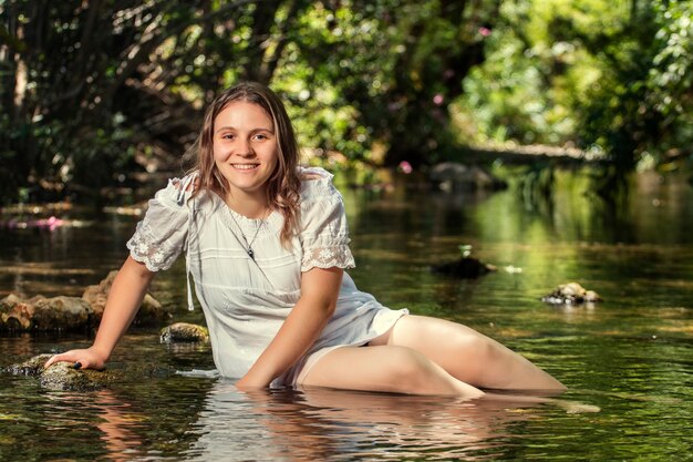 Bella giovane donna con abito bianco vicino al flusso d'acqua.