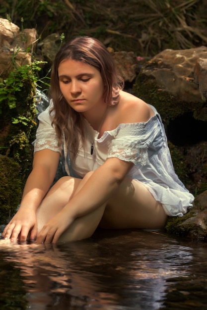 Bella giovane donna con abito bianco vicino al flusso d'acqua.