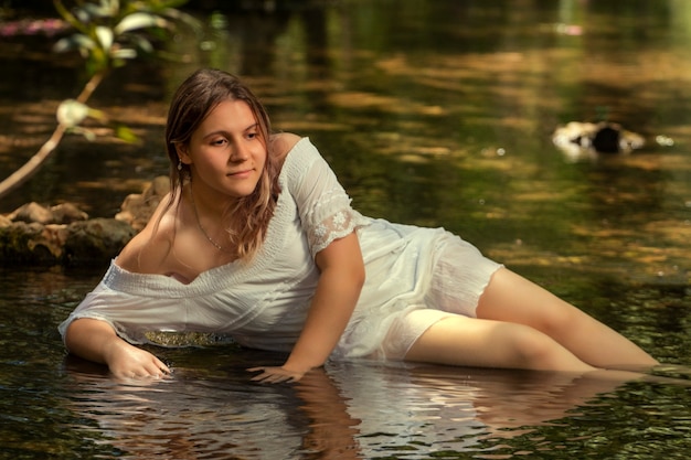 Bella giovane donna con abito bianco vicino al flusso d'acqua.