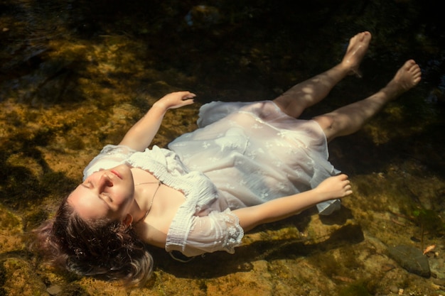 Bella giovane donna con abito bianco vicino al flusso d'acqua.