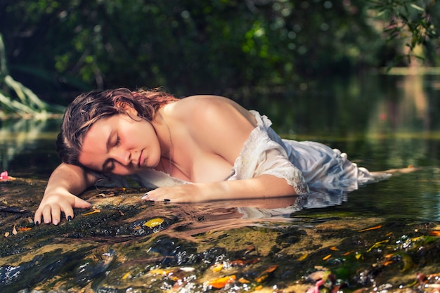 Bella giovane donna con abito bianco vicino al flusso d'acqua.