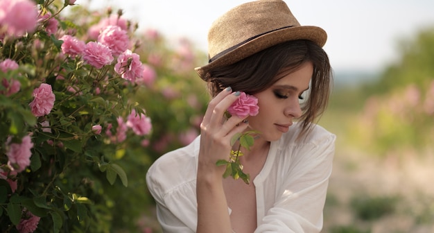 Bella giovane donna con capelli ricci che posano vicino alle rose in un giardino. Il concetto di pubblicità del profumo.