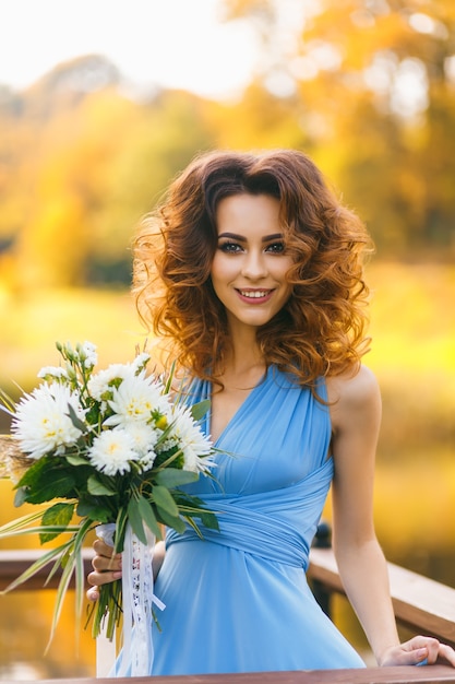 Bella giovane donna con capelli ricci lunghi che posano con il mazzo