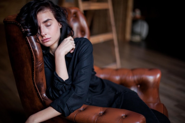 Bella giovane donna con capelli scuri ricci e trucco naturale seduto su sedie in pelle scura