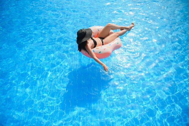 Bella giovane donna con ciambella gonfiabile in piscina blu