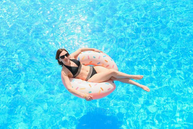 Bella giovane donna con ciambella gonfiabile in piscina blu