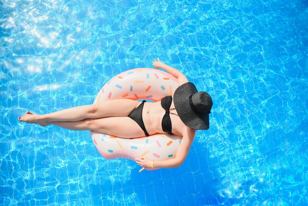 Bella giovane donna con ciambella gonfiabile in piscina blu