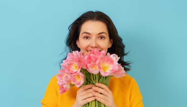 Bella giovane donna con fiori rosa tulipani in mano su sfondo blu muro