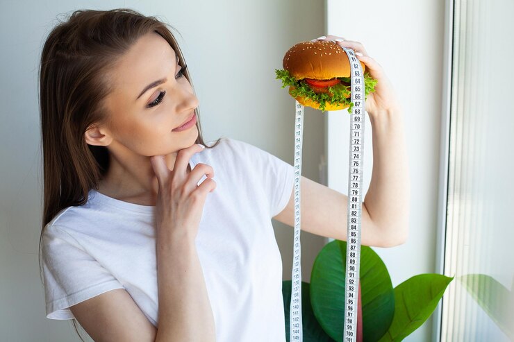 Foto bella giovane donna con hamburger e nastro adesivo di misurazione durante la dieta