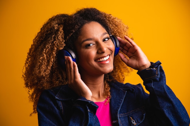 Bella giovane donna con i capelli afro che ascolta la musica con la cuffia sorridente.