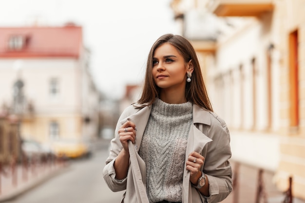 Bella giovane donna con i capelli lunghi castani in un elegante trench in posa nella città all'aperto