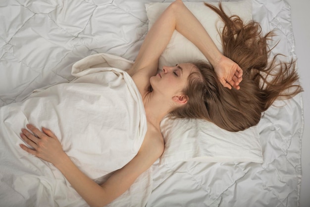 Bella giovane donna con i capelli lunghi dorme sonni tranquilli su lenzuola costose. Ritratto di vista dall'alto della ragazza addormentata.