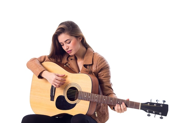 Bella giovane donna con i capelli lunghi in giacca marrone che suona la chitarra su sfondo bianco in studio