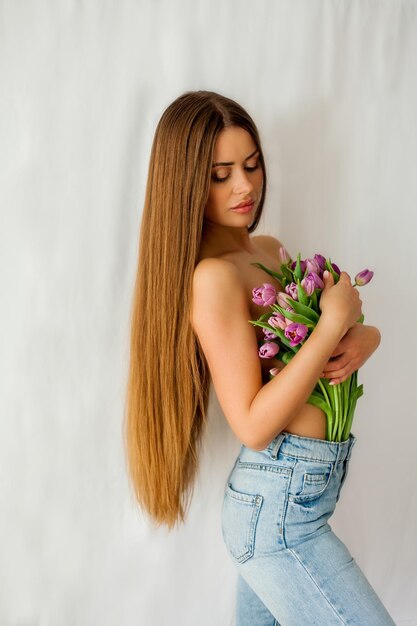 Bella giovane donna con i capelli lunghi tiene un bouquet di tulipani Ritratto di donna su sfondo bianco