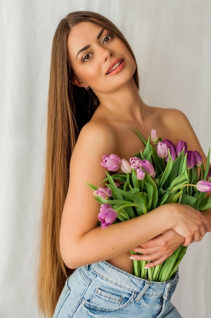 Bella giovane donna con i capelli lunghi tiene un bouquet di tulipani Ritratto di donna su sfondo bianco