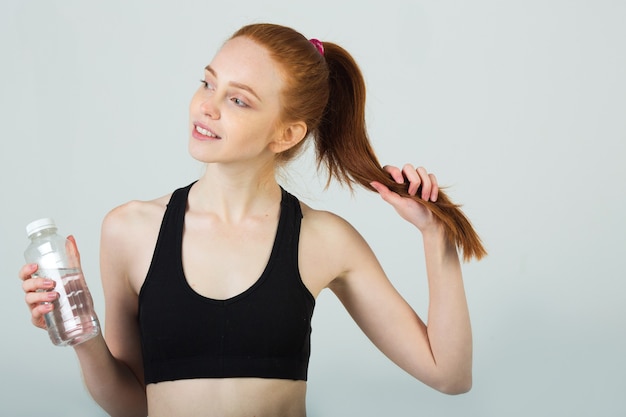 bella giovane donna con i capelli rossi in abbigliamento sportivo con una bottiglia d'acqua