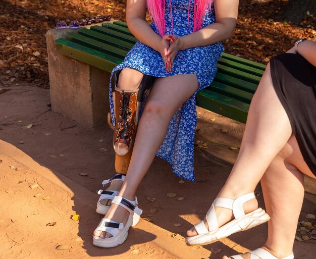 Bella giovane donna con la gamba amputata in un vestito seduta su una panchina nel parco in una giornata di sole