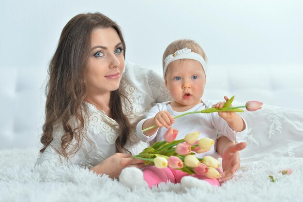 Bella giovane donna con la piccola figlia sveglia che si trova sul plaid bianco soffice