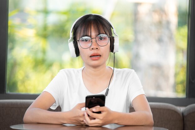 Bella giovane donna con le cuffie che si rilassano nella stanza, sta ascoltando la musica usando uno smartphone, il relax e il concetto di svago