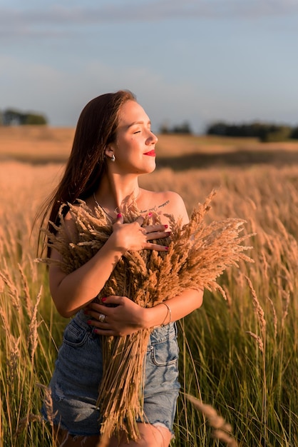 Bella giovane donna con lunghi capelli castani nel campo di grano al tramonto