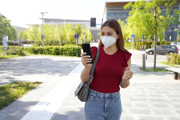 Bella giovane donna con maschera FFP2 che utilizza l'app per smartphone all'aperto