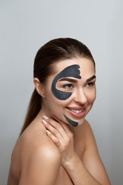 Bella giovane donna con maschera nera di argilla sul viso fresco Trattamento viso Cosmetologia bellezza