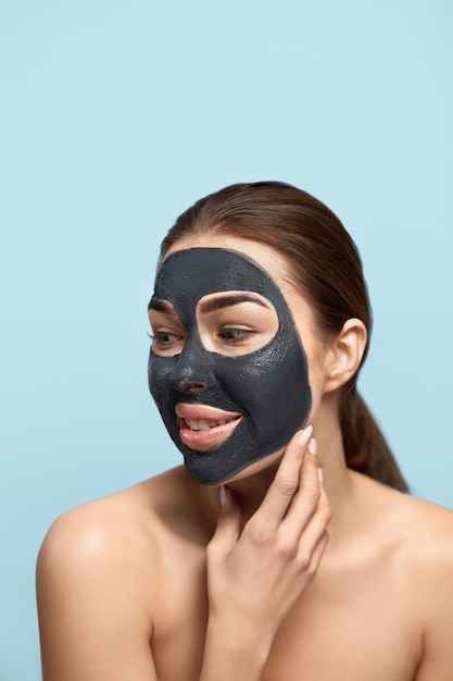 Bella giovane donna con maschera per il viso di argilla nera su pelle fresca e pulita Bellezza modello ragazza f