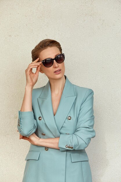 Bella giovane donna con occhiali da sole in una giacca alla moda passeggiate nel ritratto di stile di vita all'aperto della città
